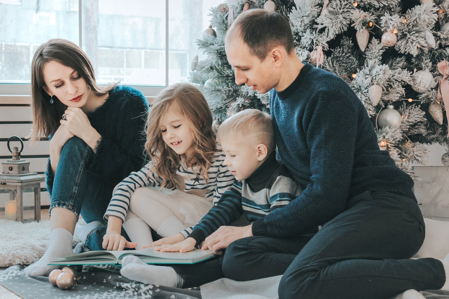 Family reading a book together by a Christmas tree.
